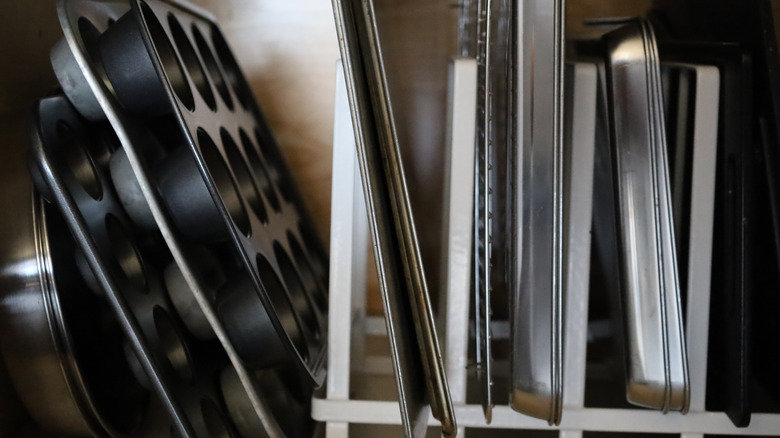 badly organized sheet pans and muffin tins in a cabinet