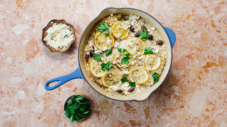 Dutch oven with baked orzo, olives, fish and lemon slices and garnishes