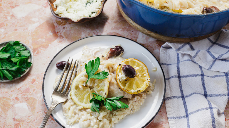 A plate with fish and orzo serving with olives beside large pot