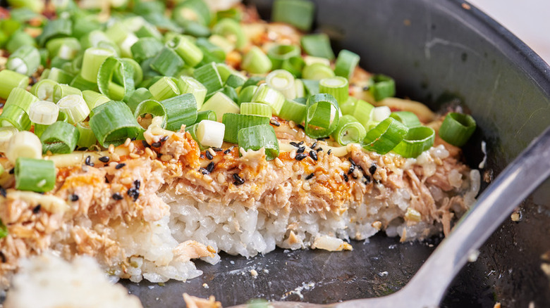 Sushi bake in baking dish, topped with salmon and chopped green onions