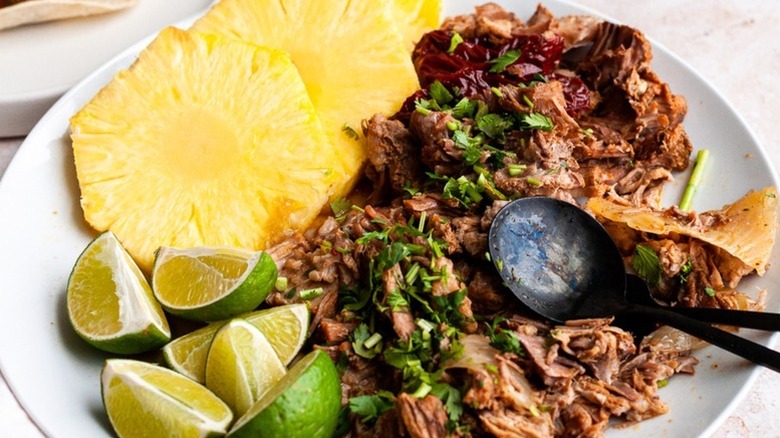 Pulled pork on plate with pineapple slices, lime wedges, and cilantro