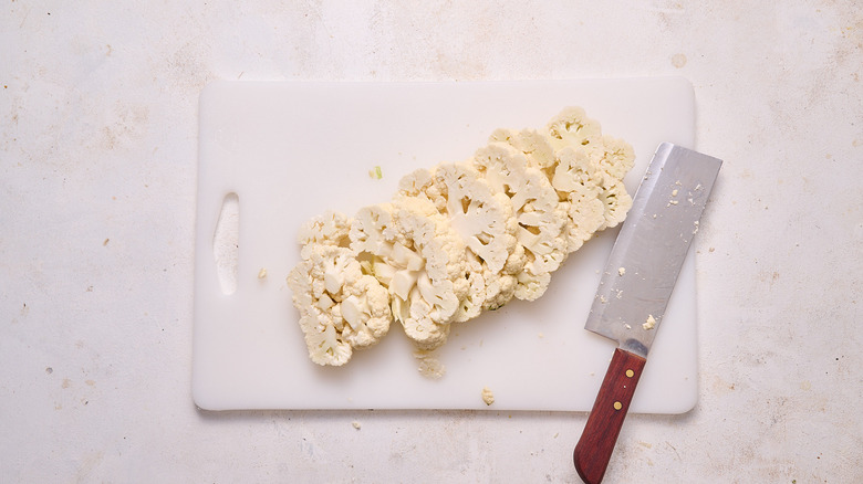 Cauliflower sliced into steaks next to knife on cutting board