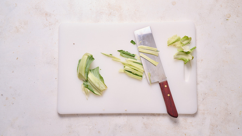 Leaves and stem of cauliflower sliced on cutting board with knife