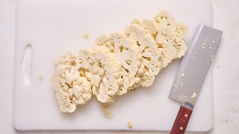 Sliced cauliflower steaks on cutting board with knife