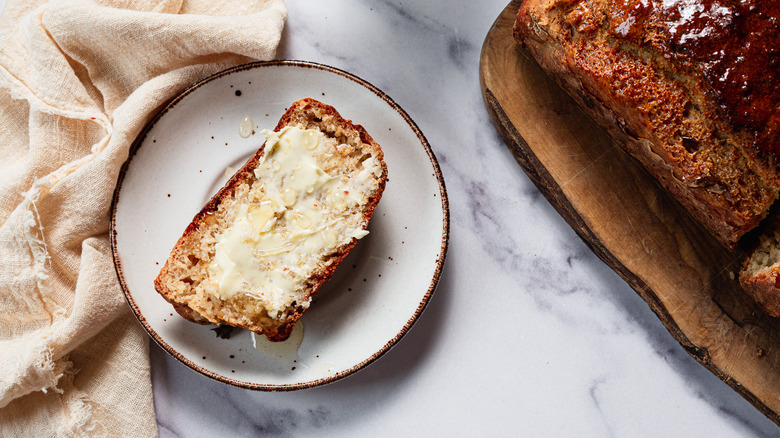 Slice of beer bread with butter on plate, wtih loaf in background