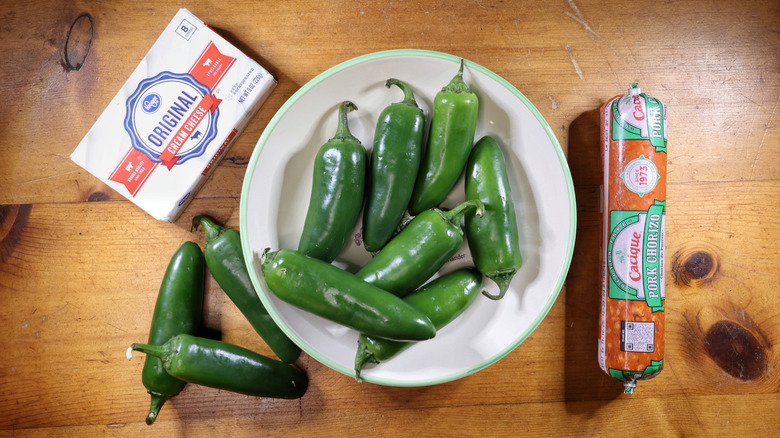 jalapeño peppers, a box of cream cheese, and a tube of pork chorizo laid out on a wooden table