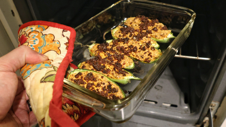 hand holding baking dish of jalapeño poppers in front of open oven