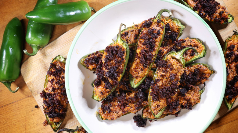 an overhead view of a plate of jalapeño poppers on a cutting board beside fresh jalapeños