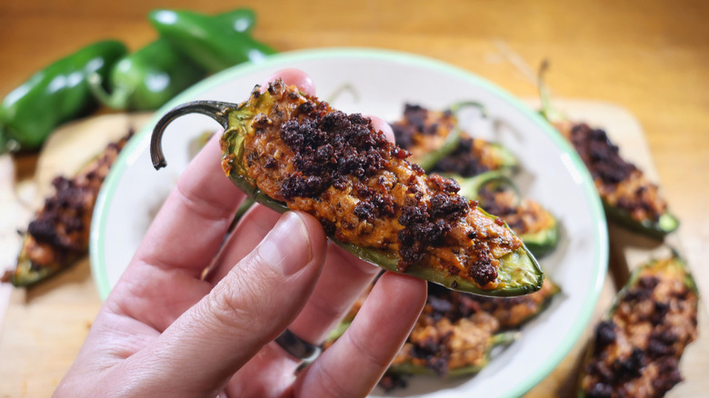 a hand holding a three-ingredient jalapeño popper above a plate of the same