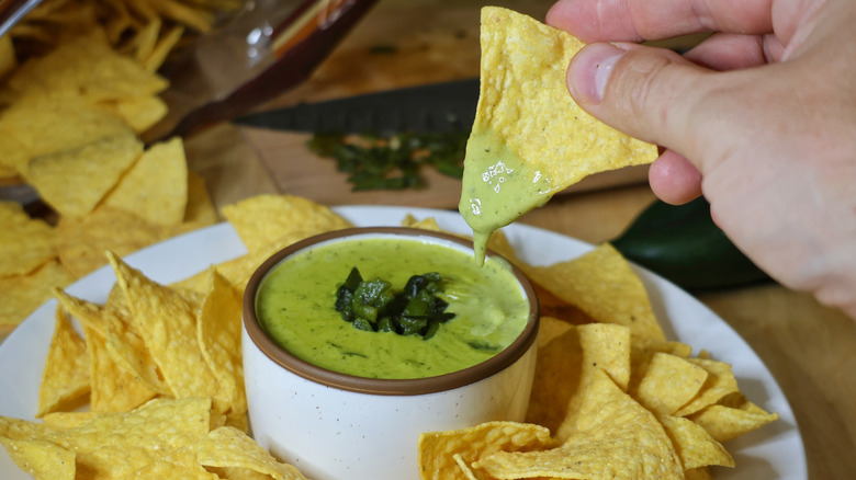 hand dipping tortilla chip into small bowl of poblano queso