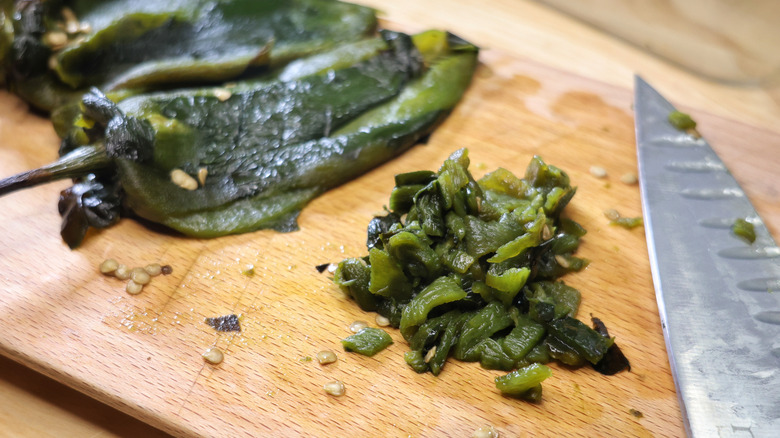 diced roasted poblanos on cutting board with knife and roasted poblano peppers