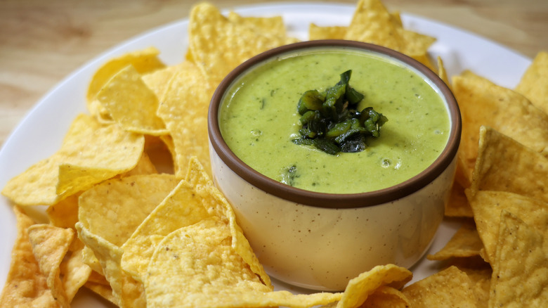 small dish of poblano queso on plate surrounded by tortilla chips