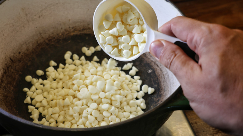white chocolate chips pouring from measuring cup into a pot on the stove