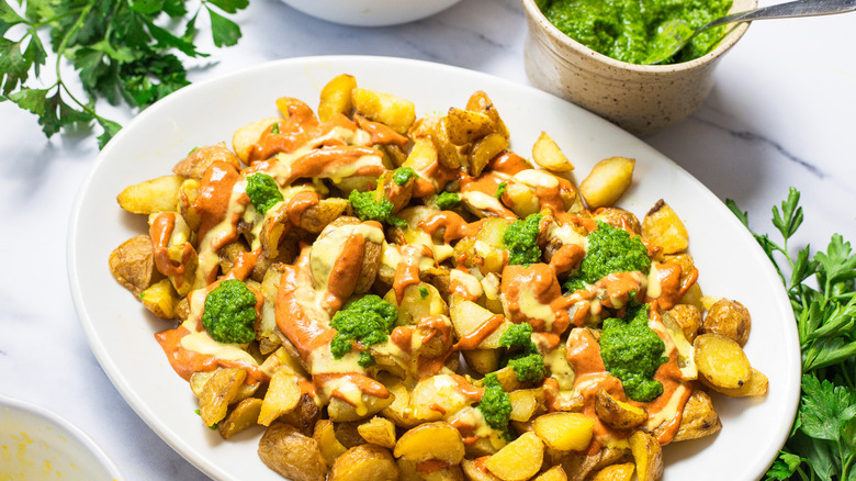 Patatas bravas surrounded by parsley and green sauce.