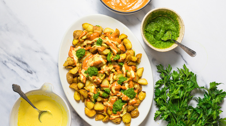 Patatas bravas surrounded by parsley and three sauces.