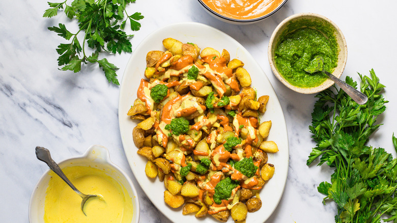 Patatas bravas surrounded by parsley and three sauces.