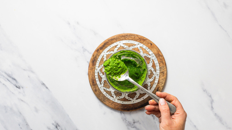 Hand lifting green parsley sauce from blender cup.