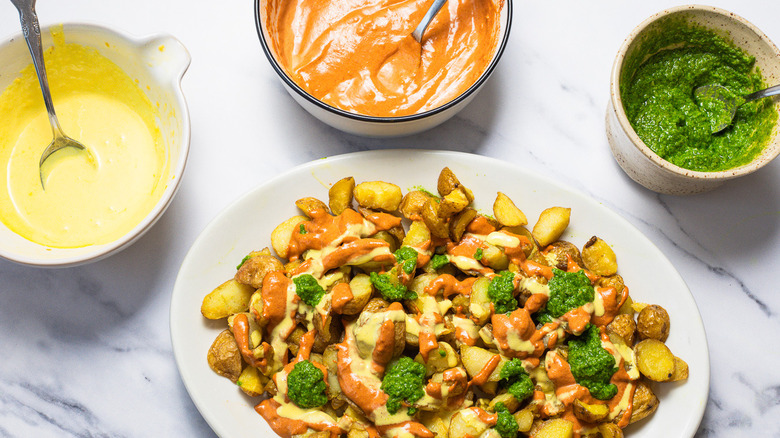 Patatas bravas surrounded by parsley and three sauces.