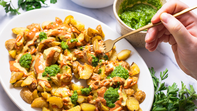 Lifting a fork with potatoes and all sauces over a platter.