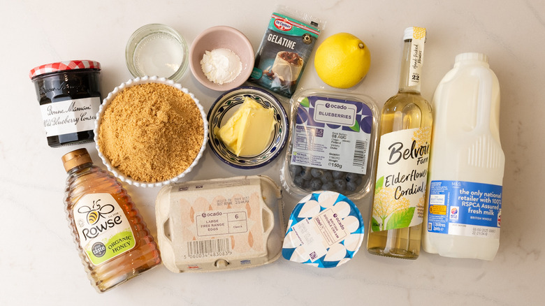 bowl of graham cracker crumbs, carton of eggs, bottle of honey, and other blueberry elderflower honeycomb pie ingredients laid out