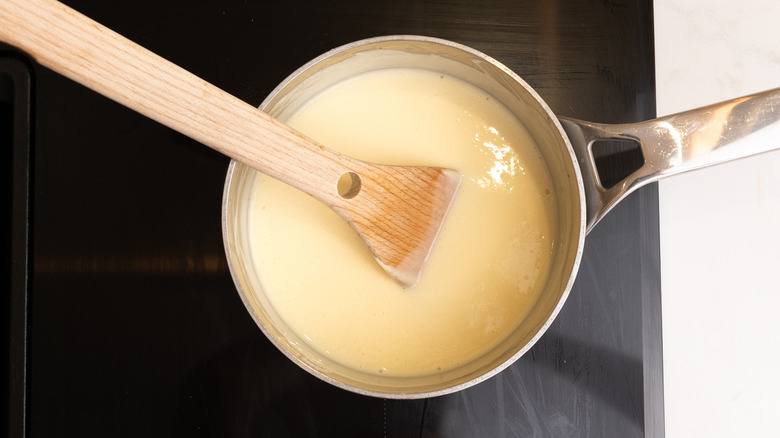 a saucepan of custard cooking on the hob with wooden spatula in it