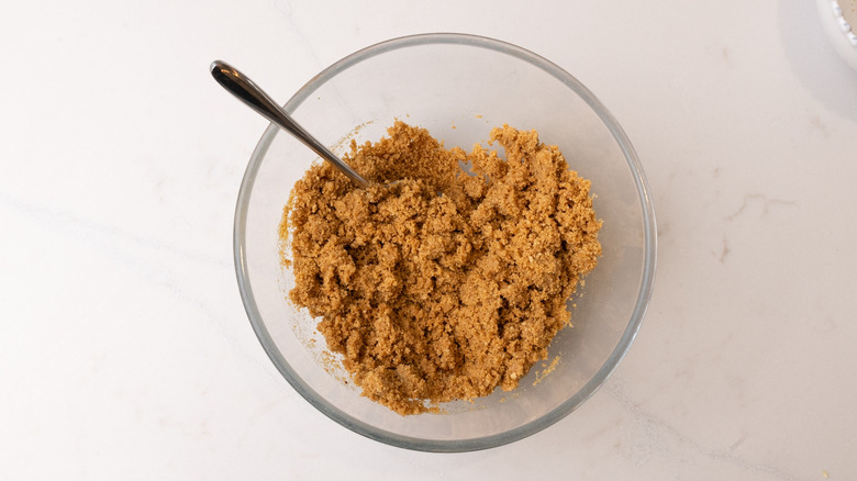 graham cracker pie crust mixture in a glass bowl with spoon inside