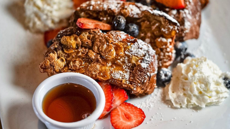 A plate of french toast, fruit, and a side of syrup