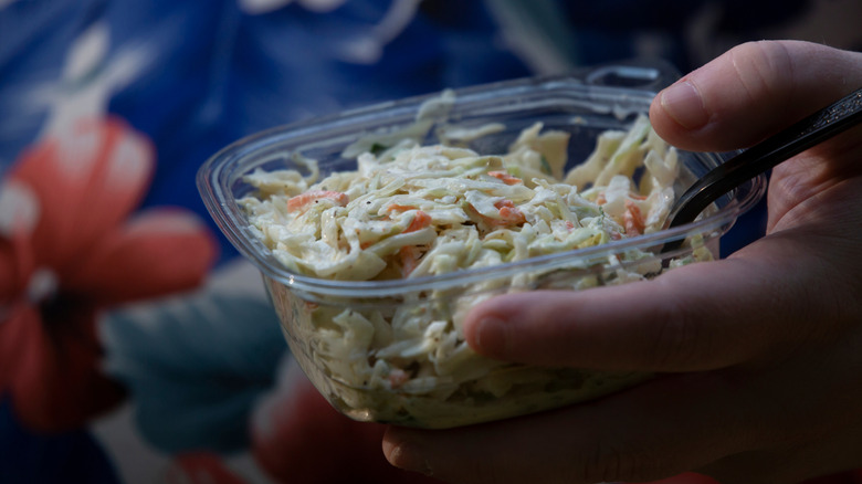 A person holding a store-bought plastic container of coleslaw