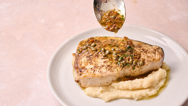spooning lemon butter sauce over swordfish steak