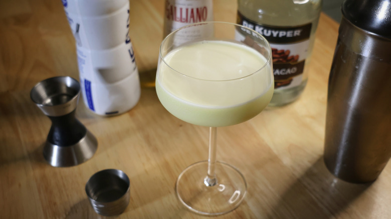 golden Cadillac cocktail on wooden table with liquor bottles and mixology equipment