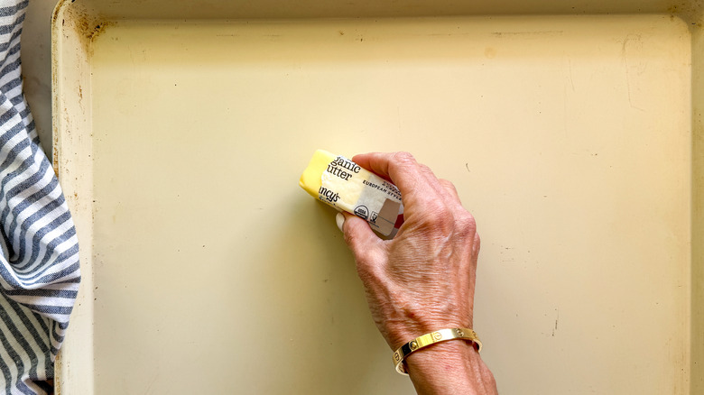 hand adding butter to baking sheet