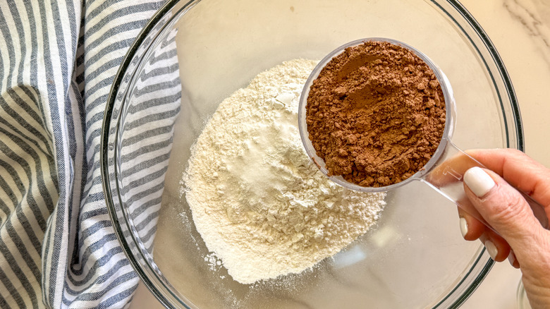 hand adding cocoa powder to bowl
