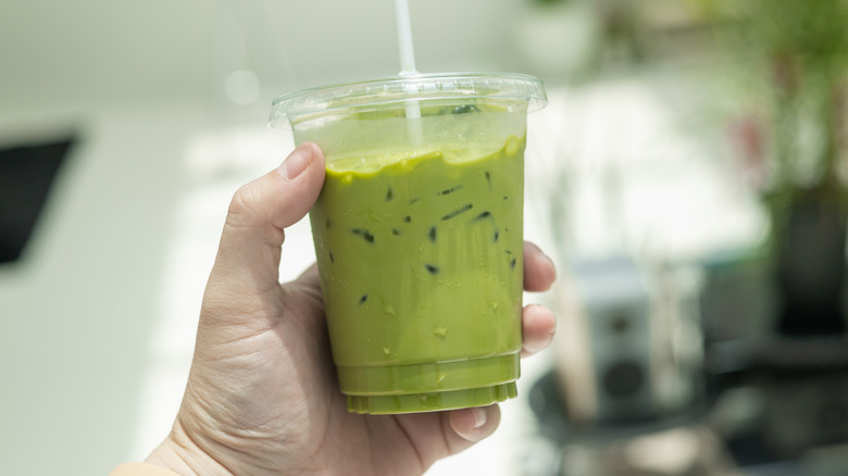 person holding iced green tea in plastic cup with a lid