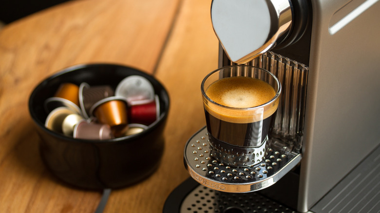 Nespresso Vertuo machine brewing coffee into cup with pods nearby