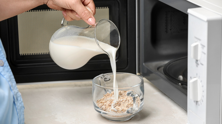 hand adding milk to oatmeal in front of a micrwoave