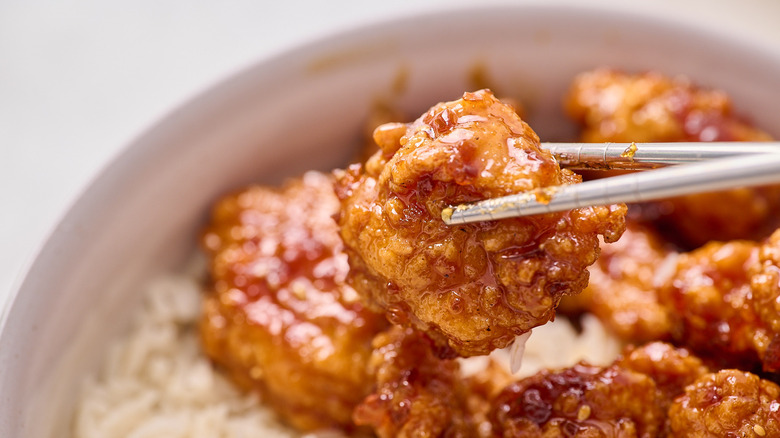 holding orange chicken with chopsticks