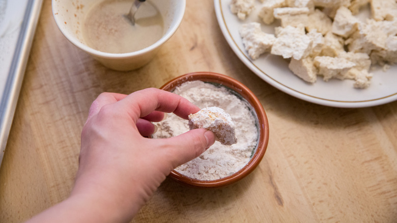 hand dredging tofu in flour