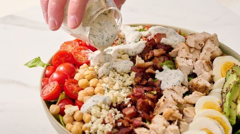 Hand pouring ranch dressing over Cobb salad