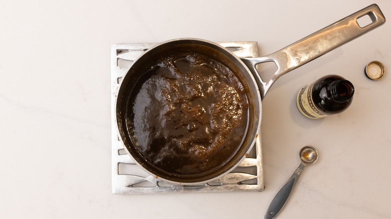 Sticky toffee sauce in saucepan next to bottle of vanilla extract