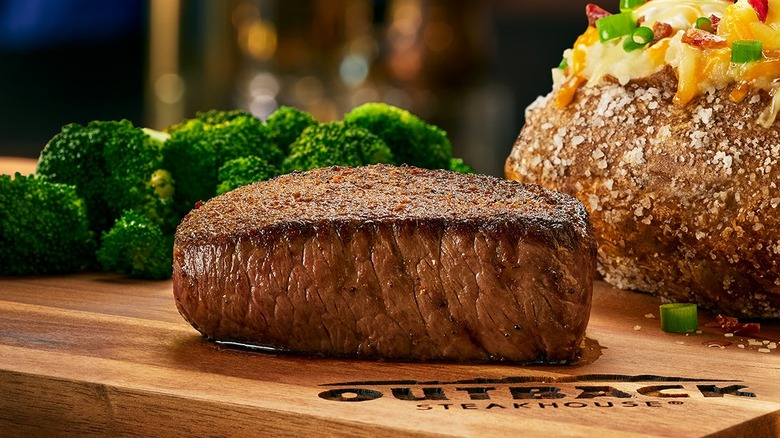 The center-cut sirloin on a wooden board that says Outback Steakhouse, with broccoli and baked potato