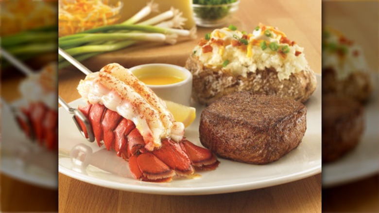 Two lobster tails plated with a mashed potato and steak