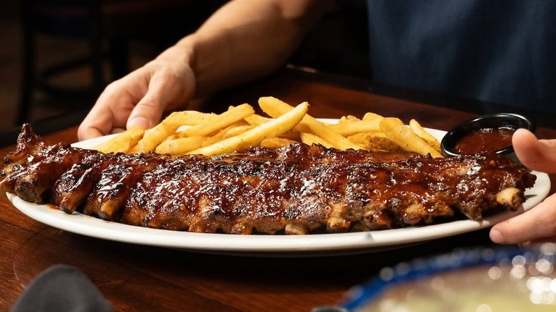 Customer holding plate with french fries and full rack of baby back ribs from LongHorn steakhouse