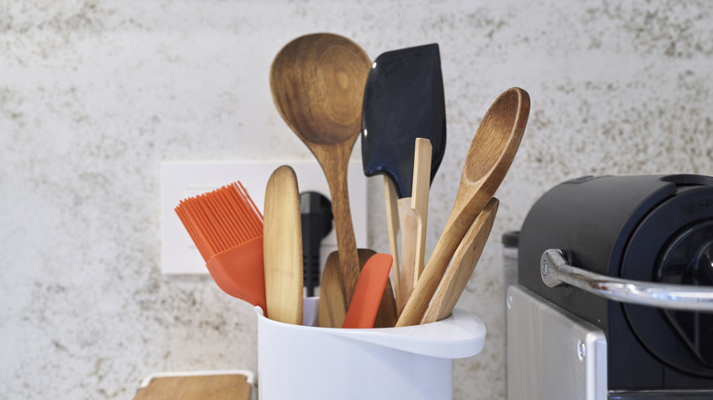 Different kitchen utensils gathered in a white holder against a white wall