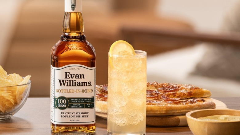 Bottle of Evan Williams Bottled-in-Bond on a table surrounded by food and a drink