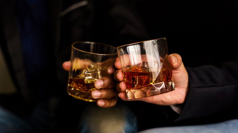 Two people clinking filled glasses of whiskey together