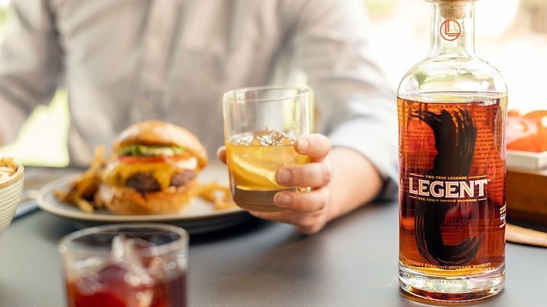 Bottle of Legent on a table with a person holding a glass in the background