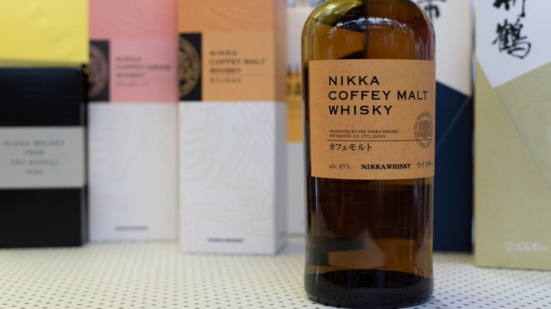 Bottle of Nikka Coffey Malt Whisky on a white shelf with blurred boxes in the background