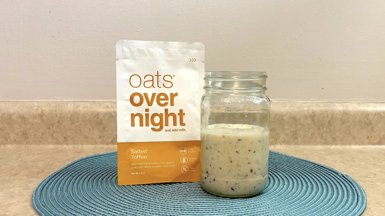 Oats Overnight salted toffee overnight oats mix in a mason jar on blue placemat, beige countertop