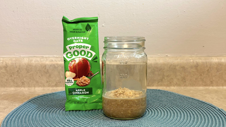 Proper Good apple cinnamon overnight oats mix in a mason jar on blue placemat, beige countertop