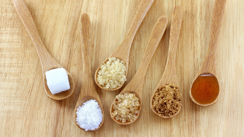 Spoons of different types of sugar on the wooden surface